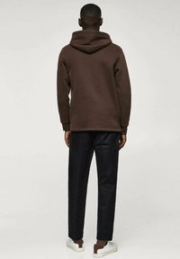 Felpa marrone con un grande cappuccio, abbinata a pantaloni neri e sneakers bianche. Il tessuto sembra morbido con un design casual.