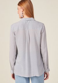 Camisa de manga larga con un estampado geométrico en blanco y azul, puños con botones y un detalle de yugo en la parte posterior, con una tela suave y ligera.