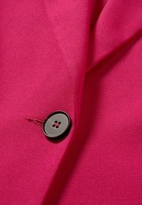 Tissu rose vif avec un gros plan d'un bouton noir à quatre trous cousu avec un fil rose assorti sur un panneau de vêtement.