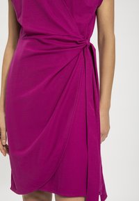 Fuksia väljakleid pehmest kangast, kätkeb endas seotud vööd ja langevat disaini, millel on sile ja tekstuurita viimistlus.