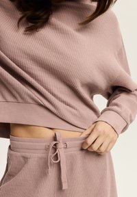 Top z długim rękawem o teksturze wafla, krótki, w delikatnym różu, w połączeniu z pasującymi wysoko taliowanymi spodniami z regulowanym pasem.