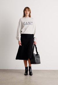 Lichtgrijze sweatshirt met "GANT" tekst, zwarte rok, zwarte enkelhakschoenen en een zwarte handtas. Gladde textuur en losse pasvorm.