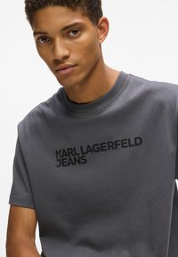 Szara bawełniana koszulka z okrągłym dekoltem i krótkimi rękawami. Na przodzie wyraźnie widoczny czarny nadruk z logo "KARL LAGERFELD JEANS".