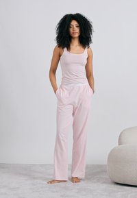 Világos rózsaszín ujjatlan felső és hozzáillő, laza fazonú pizsamanadrágok, puha anyagból készültek. A nadrág derékpántja elasztikus, és oldalzsebekkel rendelkezik.