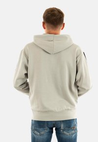 Felpa grigia chiara con cappuccio regolabile, polsini e orlo a costine. Sul retro presenta una texture liscia, con accenti scuri sulle maniche.