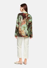 Long-sleeve blouse with a dark brown base, featuring a colorful floral and leaf print. The garment has a green checkered collar and is semi-sheer.