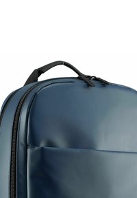Zaino blu navy con un esterno liscio e texture, dotato di due scomparti con zip e una maniglia superiore per il trasporto.