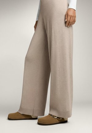 Beige wijde broek gemaakt van zachte gebreide stof, met een geribbelde tailleband. Gepaarde met bruin instap-schoenen met een gespsaccent.