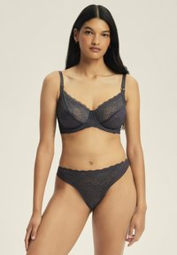 Czarny koronkowy biustonosz i stringi z falbaniastymi krawędziami, kwiatowymi wzorami i regulowanymi ramiączkami. Miękka tekstura i przezroczyste detale.