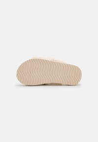 Beige slipper with a textured, cozy upper and a flexible, wavy-patterned rubber sole for traction and comfort.