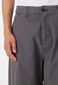 Grå, lette bukser med knaplukning og sidelommer; har en glat tekstur og discé detaljering.