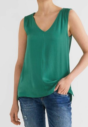 Grøn ærmeløs top med V-hals og rynkede detaljer ved skuldrene. Stoffet er glat med en løs pasform, kombineret med blå jeans.