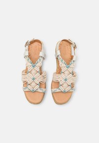 Macramé sandals featuring beige and light blue woven patterns, adjustable ankle straps, and a natural leather sole.