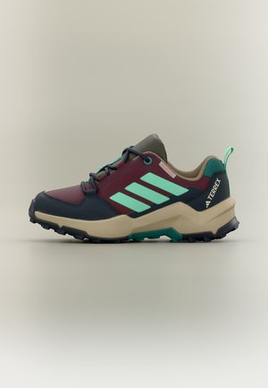 Outdoor-Wanderschuh in Bordeaux, Petrol und Beige mit dicker Sohle, drei mintgrünen Streifen und Terrex-Logo an der Fersenseite.