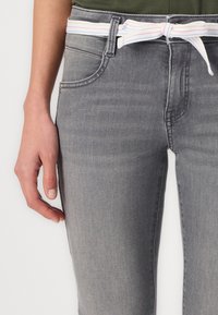 Sivi traperice slim fit, s prednjim džepovima i bijelim remenom s pastelnim prugama vezanim u struku.