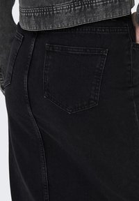 Svart jeanskjol med midjehöjd, som har en bakficka och synliga sömmar. Tyget har en slät, lätt texturerad yta.