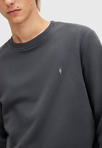 Sudadera gris oscuro con cuello redondo, puños acanalados y un sutil bordado de una calavera de cabra en el pecho. Tejido suave con una textura lisa.