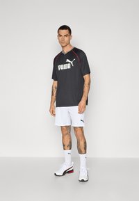 T-shirt de sport noire avec des accentuations rouges et le logo « PUMA » en blanc, associée à un short blanc avec un logo noir, des chaussettes blanches et des chaussures de sport.