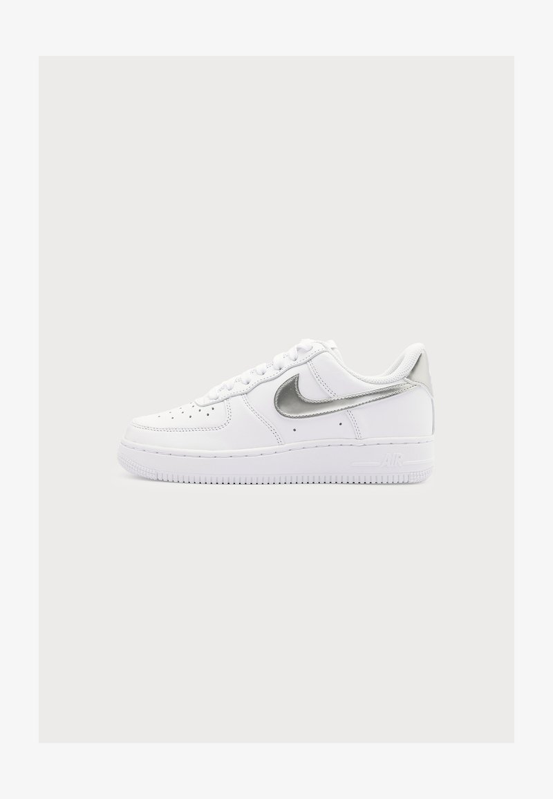 Άσπρο sneaker χαμηλού ύψους με ασημένιο λογότυπο Nike και διάτρητη μύτη, εμφανίζεται σε απλό ανοιχτό γκρι φόντο.