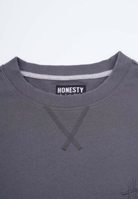 Gray sweatshirt with a ribbed crew neck, featuring tonal stitching, and "HONESTY" tag. Smooth texture with an embroidered accent detail.