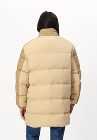 Beige dunjakke med quiltestruktur, høy krage og elastiske cuffs. Har en løs passform og mid-length design, laget av et mykt, teksturert stoff.