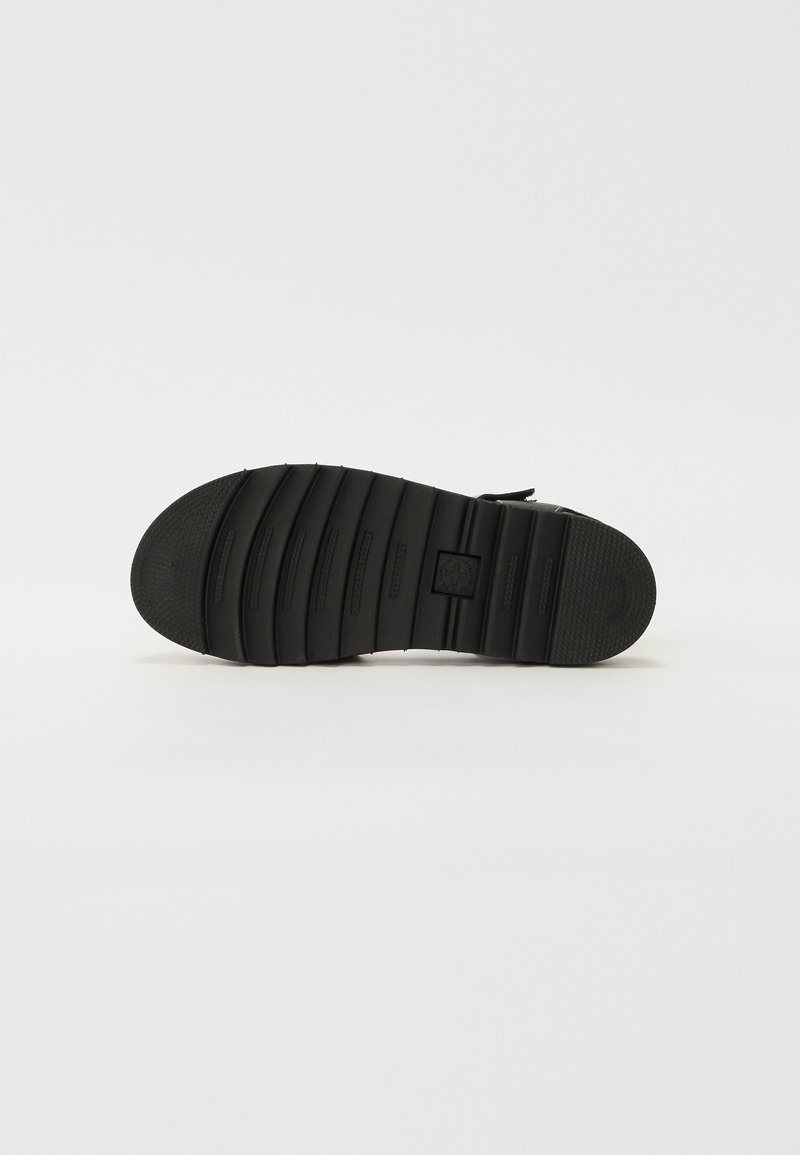 Semelle de chaussure noire avec des rainures horizontales et une surface texturée. Présente un petit logo sur la semelle intermédiaire et un design de bout arrondi.