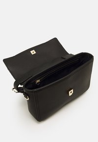 Sort lædertaske med en struktureret finish, der har en guldfarvet firkantet lås, lynlåslukket indvendigt rum og justerbar skulderrem.