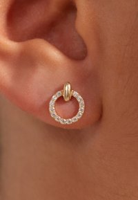 Boucles d'oreilles créoles dorées avec un motif circulaire, incrustées de petites pierres claires, attachées par un connecteur en or.
