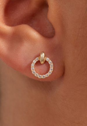 Boucles d'oreilles créoles dorées avec un motif circulaire, incrustées de petites pierres claires, attachées par un connecteur en or.