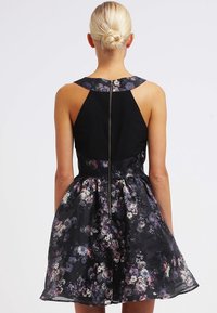 Blommig klänning med en figursydd svart kroppen och en utsvängd kjol med ett flerfärgat blommönster. Bakre dragkedjestängning och breda axelremmar.