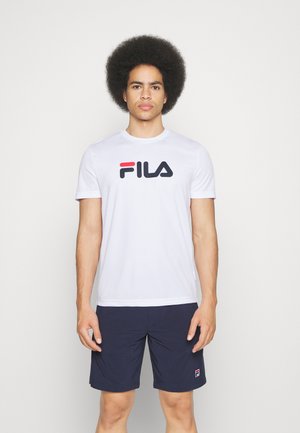 T-shirt blanc à manches courtes avec un logo FILA noir et rouge, associé à un short bleu marine portant un petit logo FILA rouge et blanc sur la jambe.