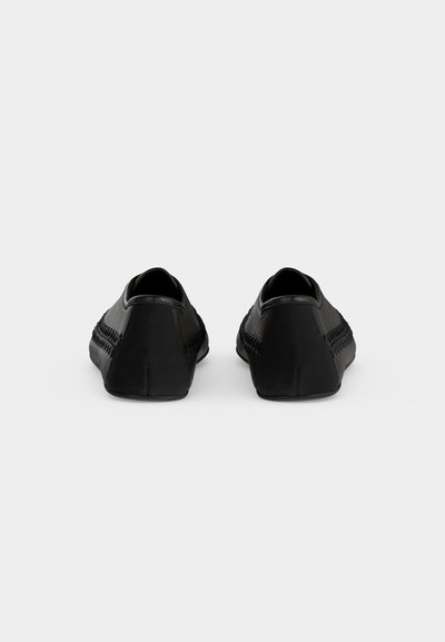 Paire de mocassins noirs sans lacets vue de dos sur un fond uni gris clair.
