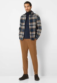 Skjorte i ternet bomuldsflannel i blå, grå og brun; tætsiddende navy turtleneck; brune tapered bukser; mørke ruskind ankelstøvler med tykke såler.