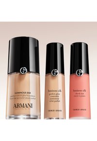 Drei Giorgio Armani Luminous Silk Make-up-Flaschen mit schwarzen Verschlüssen: Foundation, Concealer und Korallenfarbener Rouge-Tint vor hellem Hintergrund.