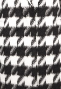 Uldfrakke med et stort hundetandsmønster i sort og hvid, med en blød, lidt fuzzy tekstur og et struktureret design.