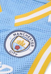 Világoskék hálós poliészter anyagú mez, kör alakú Manchester City logóval, sárga és fehér csíkokkal díszítve a nyakrésznél.