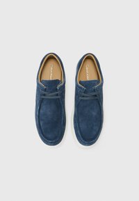 Mørkeblå sneaks i suede med rund tå, hvit såle og minimalistisk snøring. Innvendig har de en lysebrun innersåle med merke.