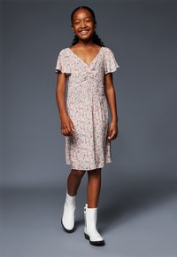 Blumenmusterkleid mit V-Ausschnitt, weichem Stoff, kurzen, flatternden Ärmeln und geraffter Taille. Getragen mit weißen Knöchelstiefeln und dunkler Sohle.