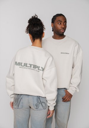 Two people wearing white sweatshirts with "MULTIPLY" text, one facing forward, the other showing the back logo, standing against a plain background.