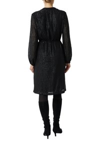 Czarna sukienka z pionowymi, błyszczącymi paskami, długimi przejrzystymi rękawami, elastyczną talią oraz długością do kolan. W połączeniu z czarnymi kozakami za kolano.