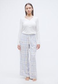 Μακρυμάνικη λευκή μπλούζα henley συνδυασμένη με ανοιχτόχρωμο καρό πιτζάμα παντελόνι με μπλε και μπεζ γραμμές και μικρές λουλουδάτες λεπτομέρειες. Απαλή υφή υφάσματος.