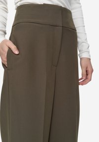 Hoge taille, wijd uitlopende broek in olijfgroene stof, met voorplooien en zijzakken, gecombineerd met een getailleerd wit topje.