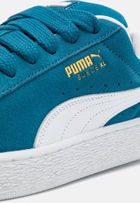 Baskets en daim bleu sarcelle avec accents en cuir blanc et semelle en caoutchouc texturée. Comprend des lacets tissés et des détails de logo dorés.