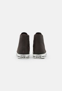 Brązowe zamszowe trampki typu high-top z białymi gumowymi podeszwami i czarnym logo na pięcie. Posiadają naszywkę z logo po boku.