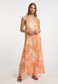 Rochie lungă de culoare portocalie, cu modele florale și paisley. Dispunând de bretele subțiri, ajustabile și un tiv în straturi. Asortată cu sandale plate maro.