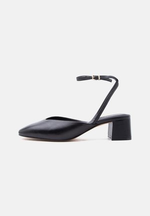 Schwarzer Leder-Pumps mit niedrigem Blockabsatz, spitz zulaufender Schuhspitze und dünnem Knöchelriemen mit goldener Schnalle vor hellem Hintergrund.