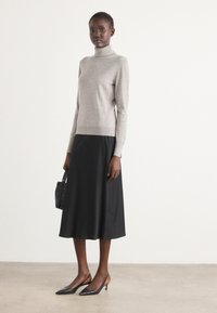 Grå rullekravesweater, sort midi-nederdel og sorte slingback-sko med beige accenter. Lille struktureret sort håndtaske. Enkel og elegant design.