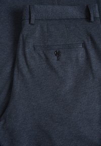 Pantalon gris foncé sur mesure avec passants de ceinture et une poche arrière unique avec bouton, fabriqué en tissu texturé.