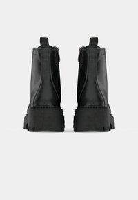 Stivaletti neri alla caviglia con finitura in pelle liscia, suola solida e rialzata, e chiusura con zip laterale. Presenta linguette sul retro per una facile calzata.