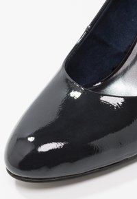 Escarpin en cuir verni noir avec un bout pointu et une finition lisse et brillante. Comprend une doublure argentée et une texture intérieure confortable.